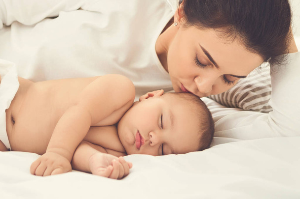 Mère embrassant son nouveau-né endormi au lit
 - Photo, image