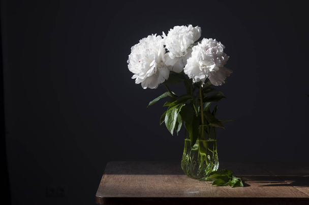 bouquet of white peonies in a transparent vase on a dark background - Foto, imagen