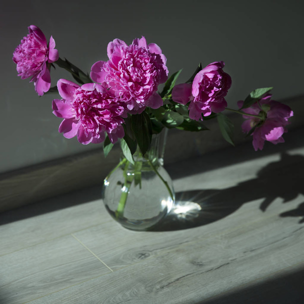 Bouquet of pink peonies in a glass transparent vase on the floor - Fotó, kép