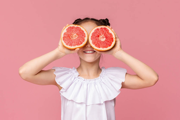 Cute girl holding grapefruit slices near her eyes - Fotografie, Obrázek