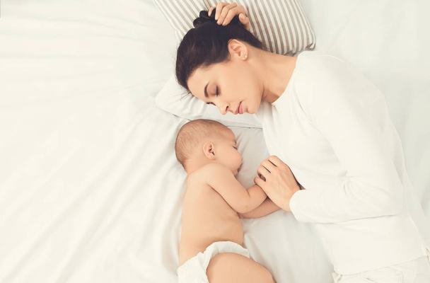 Jovem mãe e seu bebê bonito dormindo na cama
 - Foto, Imagem