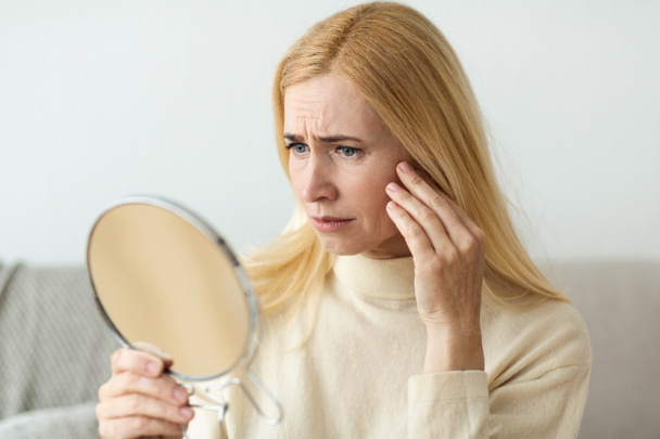 Cuidado de la piel anti-arrugas. Triste mujer mirando en el espejo
 - Foto, imagen