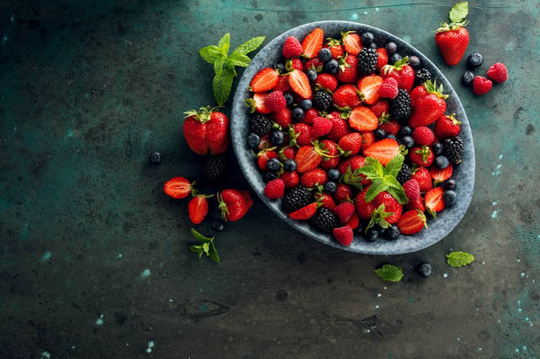 top view of fresh ripe berries in bowl on grey surface  - Foto, Bild