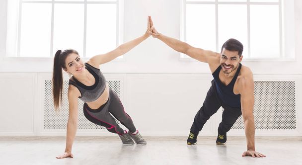 Active couple standing in plank and giving high five with one ha - Zdjęcie, obraz