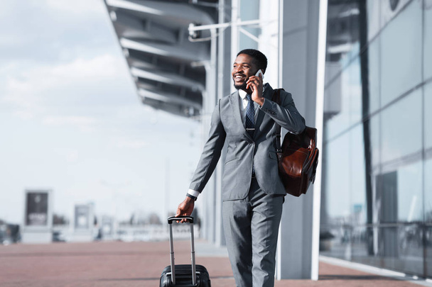 Afrikaanse man lopen met bagage en praten op telefoon - Foto, afbeelding