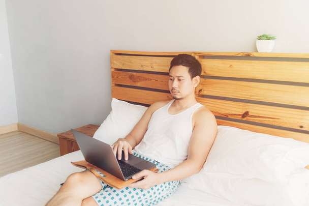L'homme seul travaille avec son ordinateur portable sur son lit confortable. Concept de mode de vie au travail indépendant
. - Photo, image