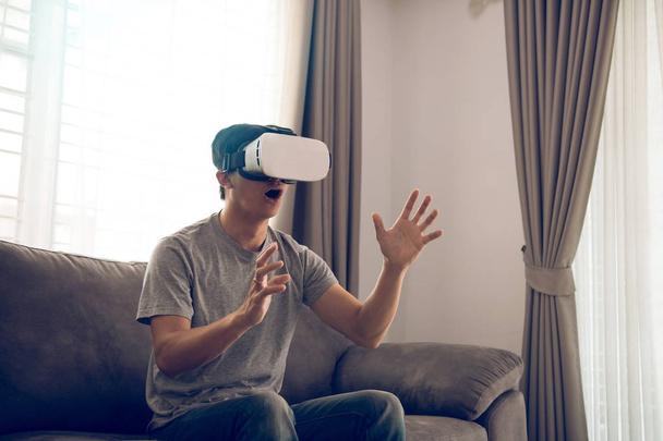 Nuori aasialainen mies yllään virtuaalitodellisuus lasit olohuoneessa f
 - Valokuva, kuva