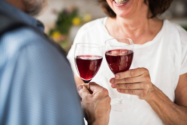 A midsection of senior couple in love indoors at home, clinking wine. - Foto, afbeelding