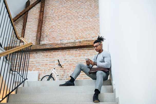 Young mixed race businessman with telephone sitting on stairs in office building. - Фото, изображение