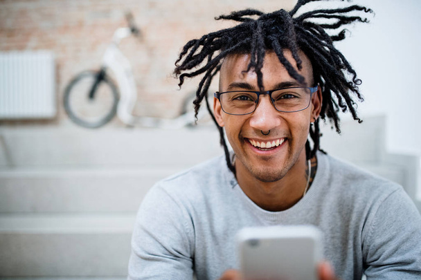 A young mixed race businessman with dreadlocks and smartphone in office. - Foto, imagen