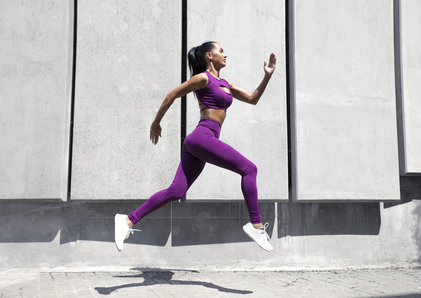 Sportos női futó dinamikus mozgásban. Fitt és egészséges lány edzés az utcán. Testedzés. Fitness női divatos ruhák gyakorlása.  - Fotó, kép