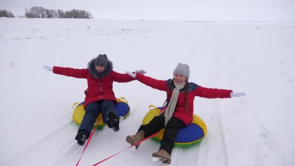 Girls go to snow saucer on white snowy road and laugh with pleasure. Winter fun cheerful teenagers on frosty day - Footage, Video
