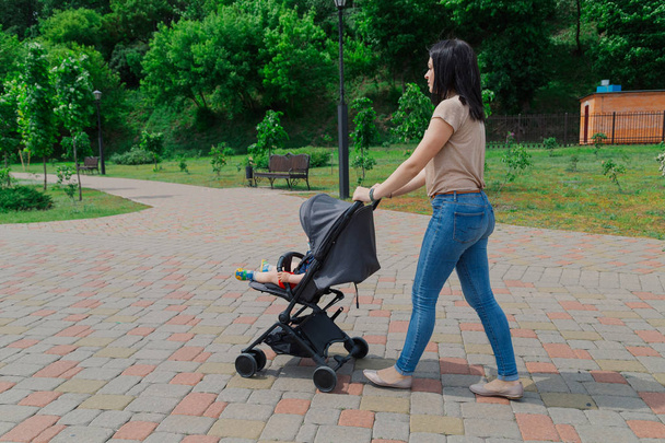 Красивая женщина с ребенком в коляске гуляет по летнему парку
. - Фото, изображение
