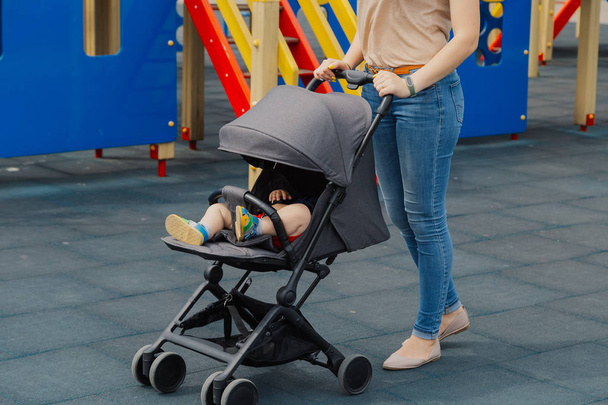 Young mom with a baby in a stroller at the playground. - Fotografie, Obrázek