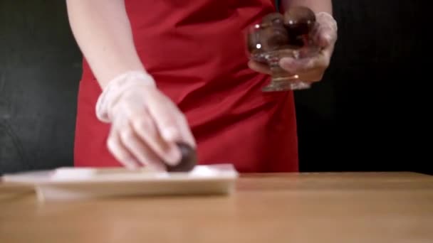 Makadamiapähkinöitä lautasella. Toimintaa. Lähikuva nainen esiliina laittaa kolme macadamia pähkinät näytteen musta eristetty tausta
 - Materiaali, video