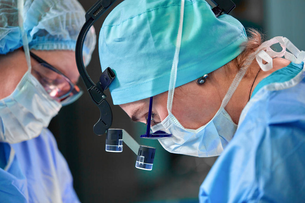 Retrato de cerca de la doctora cirujana usando máscara protectora y sombrero durante la operación. Salud, educación médica, concepto de cirugía
. - Foto, Imagen