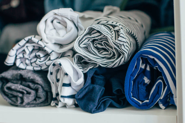 Marie Kondo με την έννοια της μεθόδου-διπλωμένα ρούχα. Άσπρα, γκρίζα, μπλε και ριγέ μπλουζάκια. Επιλεκτική εστίαση - Φωτογραφία, εικόνα