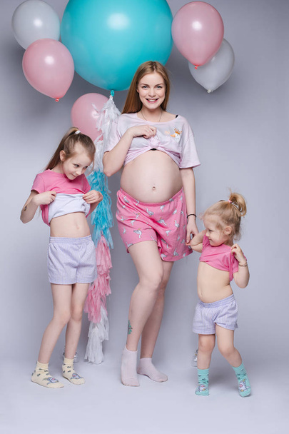 Забавное фото великолепной беременной матери с двумя дочерьми, смотрящими на свои животы
. - Фото, изображение