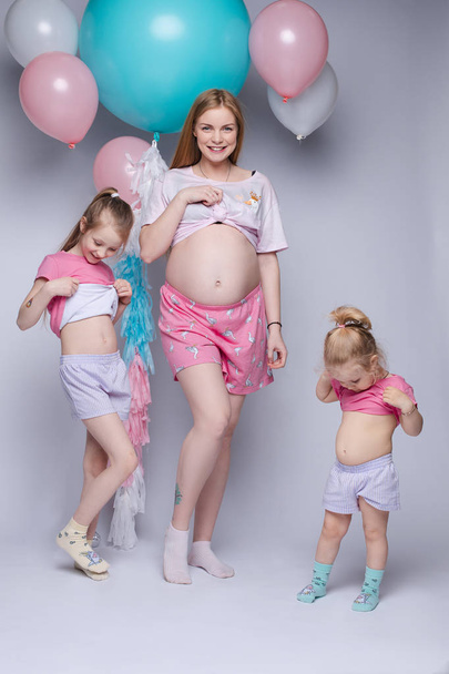 Funny photo of gorgeous pregnant mother with two daughters looking at their bellies. - Photo, Image