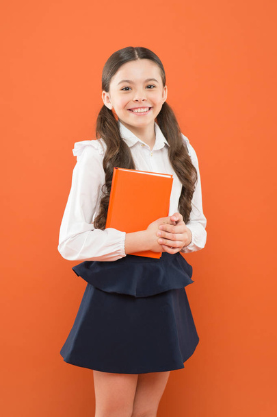 schoolgirl writing notes on orange backdrop. small girl in school uniform. reading lesson. information form book. back to school. happy child concentrated on work. Lesson at school. Smart school girl - 写真・画像