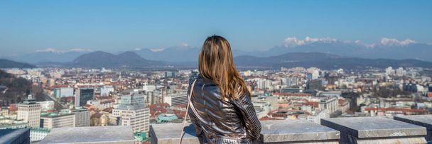 View from behind of a woman standing on top of Ljubljana castle - Foto, Imagem