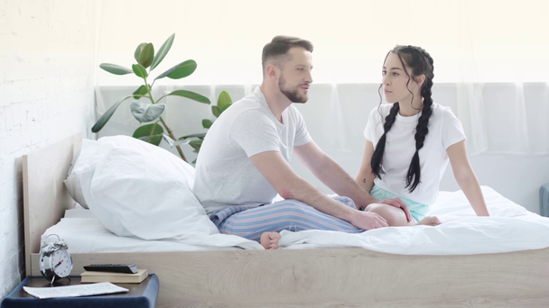 cheerful young woman smiling while talking with man and sitting on bed  - Materiał filmowy, wideo