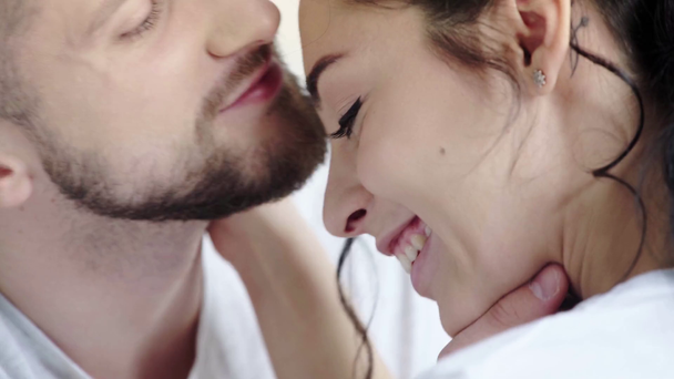 selektivní zaměření veselého muže dotýkání se vlasů a líbání šťastné bruneté ženy izolované na bílém   - Záběry, video