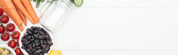 top view of tasty vegetables near glass jar on wooden white table with copy space, panoramic shot - Fotó, kép