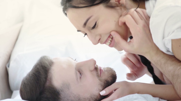 happy bearded man kissing cheeks and nose of attractive brunette girl in bedroom  - Filmati, video