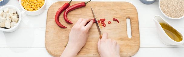 bijgesneden beeld van de vrouw snijden Chili pepers op houten hakken Board op witte tafel, panoramische schot - Foto, afbeelding
