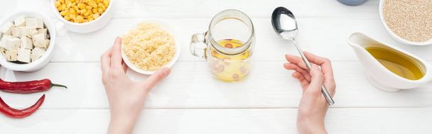 cropped view of woman holding bowl with couscous near glass jar on wooden white table, panoramic shot - Photo, Image