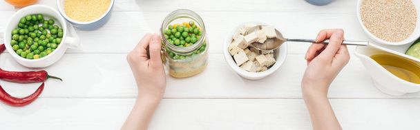 cropped view of woman adding tofu cheese in jar with salad on wooden white table, panoramic shot - Photo, Image