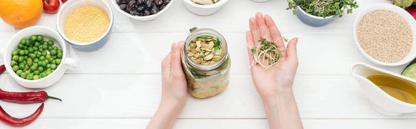 cropped view of woman adding sprouts in jar with salad on wooden white table, panoramic shot - Photo, Image