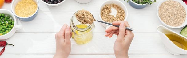 cropped view of woman adding couscous in jar with oil on wooden white table, panoramic shot - Photo, Image