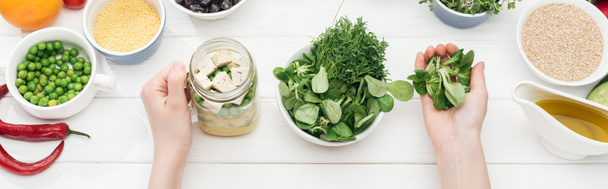 cropped view of woman adding greens in jar with tofu cheese on wooden white table, panoramic shot - Photo, Image