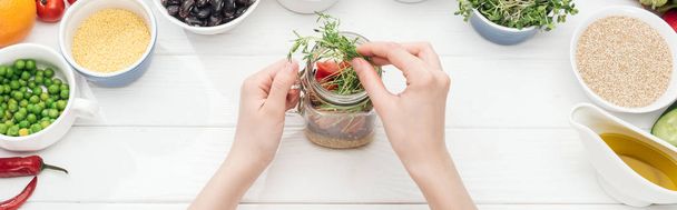 cropped view of woman adding green sprouts in jar with salad on wooden white table, panoramic shot - Φωτογραφία, εικόνα