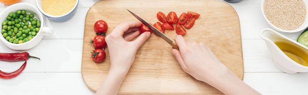 partial view of woman cutting cherry tomatoes on wooden chopping board, panoramic shot - 写真・画像