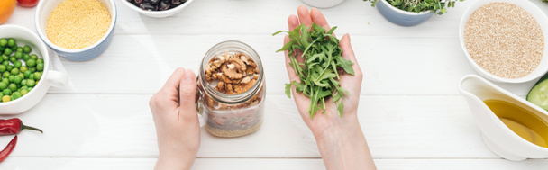 cropped view of woman adding sprouts in jar with nuts on wooden white table , panoramic shot - Φωτογραφία, εικόνα