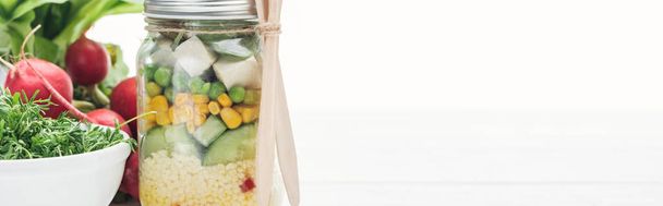 白に分離された大根の近くのガラス瓶の新鮮な野菜サラダのパノラマショット - 写真・画像