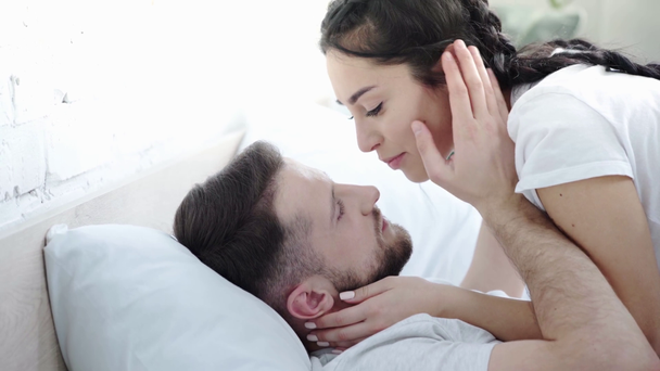 Wesoła kobieta dotykając twarzy i Całowanie czoło szczęśliwego Brodatego chłopaka leżącego na łóżku  - Materiał filmowy, wideo