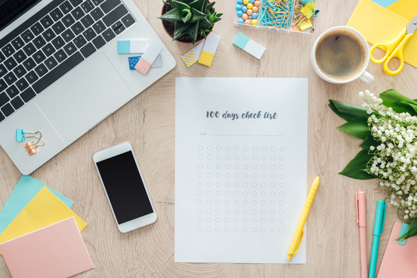 Ansicht von 100 Tagen Checkliste mit Smartphone, Laptop und Schreibwaren auf Holztisch - Foto, Bild