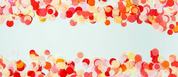 パステル調の背景に赤とオレンジのお祝いの紙吹雪で作られたカラフルなフレーム  - 写真・画像