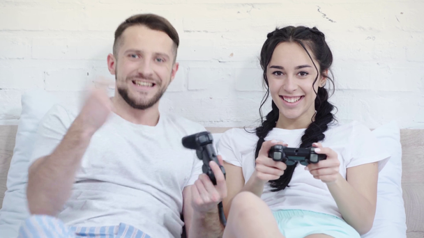KYIV, UKRAINE - MARCH 21, 2019: happy man gesturing while playing video game and winning near attractive woman in bedroom  - Πλάνα, βίντεο