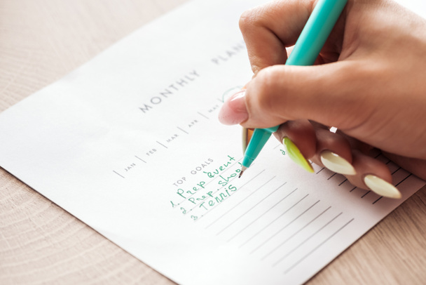 обрізаний вид жінки, що пише нотатки на щомісячному планувальнику, тримаючи зелену ручку в руці
 - Фото, зображення
