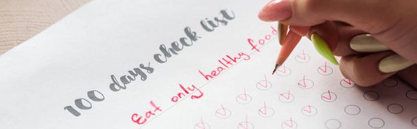 περικομμένη όψη της γυναίκας γράφοντας σημειώσεις σε 100 ημέρες λίστα ελέγχου, κρατώντας την Κόκκινη πένα στο χέρι - Φωτογραφία, εικόνα