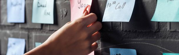 abgeschnittene Ansicht von Frau befestigen bunte Aufkleberblöcke mit Notizen an schwarzer Ziegelwand - Foto, Bild