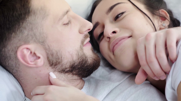 close-up de homem feliz tocando rosto e cabelo da mulher alegre enquanto se beija e deitado na cama
  - Filmagem, Vídeo