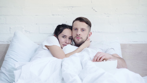 scared woman watching movie near handsome boyfriend eating popcorn in bedroom  - Footage, Video