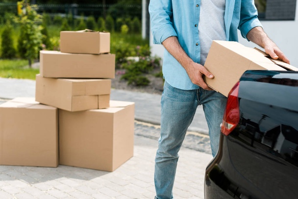 cropped view of man standing near car while putting box  - Foto, imagen