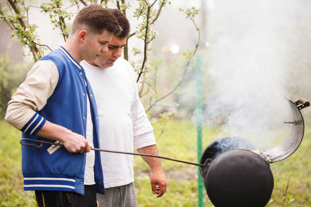 Twee jonge mannen staande in de buurt van barbecue grill. Haardvuur in de open lucht. - Foto, afbeelding